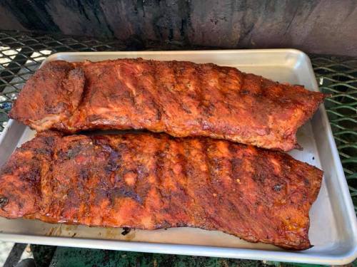 Two large, smoked pork ribs on a metal tray, showcasing a rich, dark glaze and grill marks.