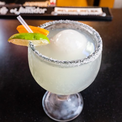 A refreshing margarita in a glass with a salted rim, garnished with lime and orange slices.