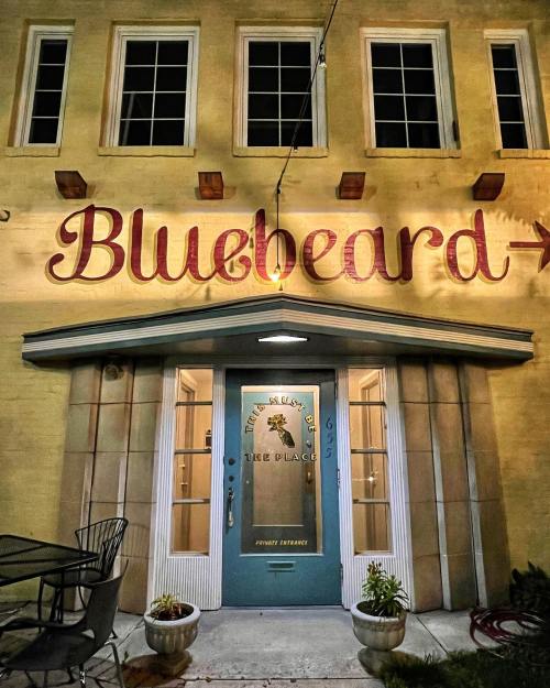 A building exterior featuring a large "Bluebeard" sign above a blue door with decorative details and outdoor seating.