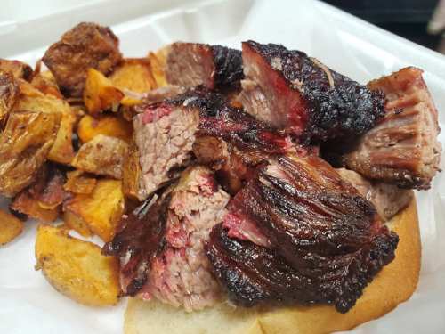 A plate of sliced smoked brisket served with golden-brown roasted potatoes on the side.
