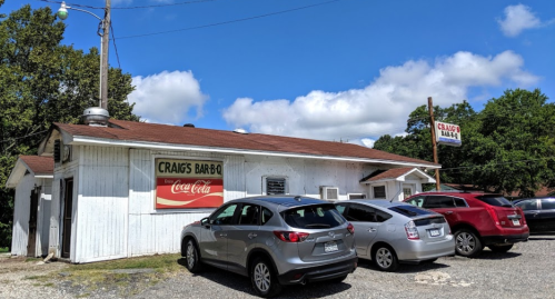 A small barbecue restaurant with a sign reading "Craig's Bar-B-Q," featuring parked cars and a blue sky.