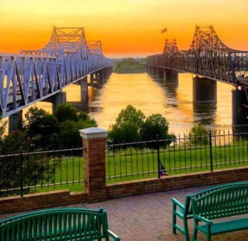 Sunset view of two bridges spanning a river, with lush greenery and benches in the foreground.