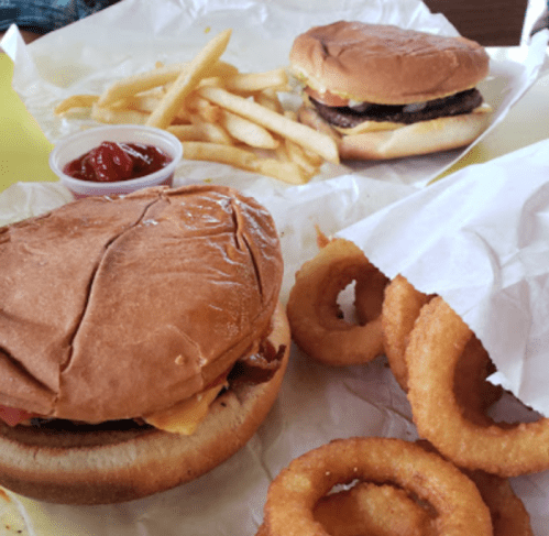 Two burgers with fries and onion rings on a table, accompanied by a small cup of ketchup.