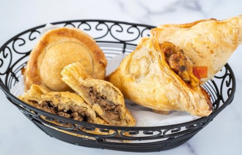 A black basket filled with various savory pastries, including empanadas and meat-filled pastries, on a marble surface.