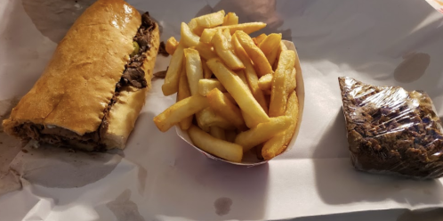 A sandwich filled with meat, a side of golden fries, and a small wrapped dessert on a white paper background.