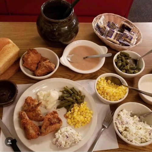A hearty meal featuring fried chicken, green beans, corn, coleslaw, mashed potatoes, and bread, with dessert on the side.
