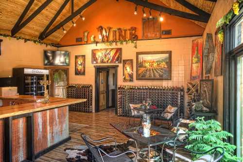 Cozy wine tasting room with a wooden bar, wine racks, artwork, and seating area under a rustic ceiling.