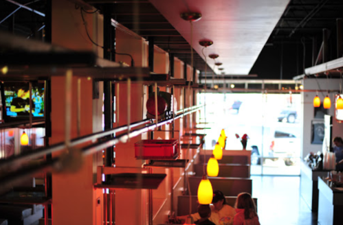 Interior of a modern restaurant with overhead lighting, booths, and a view of the entrance.