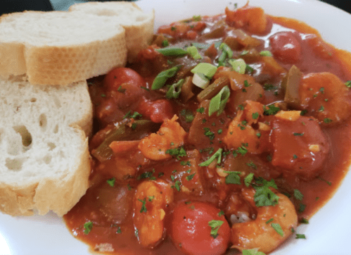 A plate of shrimp stew with tomatoes and green peppers, served with slices of bread on the side.