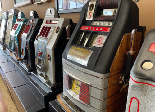 A row of vintage slot machines with various designs and colors, displayed against a wall.