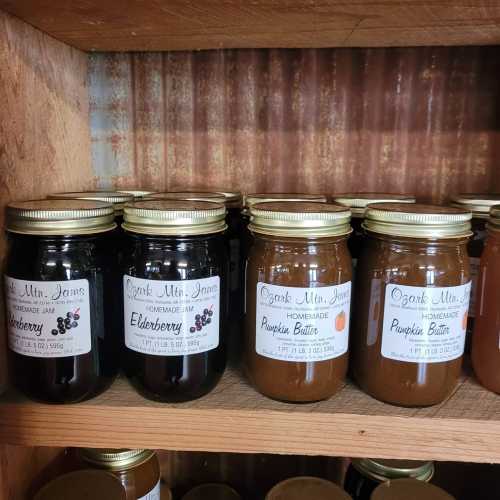 A wooden shelf displaying jars of homemade elderberry jam and pumpkin butter.