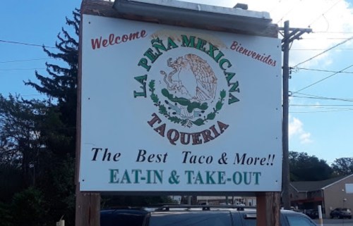 Sign for La Peña Mexicana Taqueria, featuring a welcoming message and promoting eat-in and take-out options.