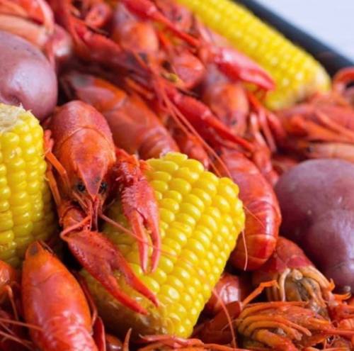 A vibrant seafood platter featuring red crawfish, yellow corn, and purple potatoes.