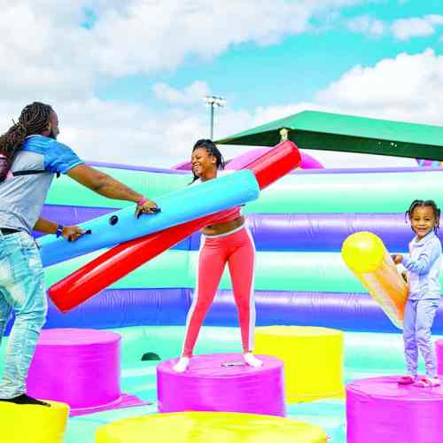 A family plays on colorful inflatable obstacles, laughing and having fun in a vibrant outdoor setting.