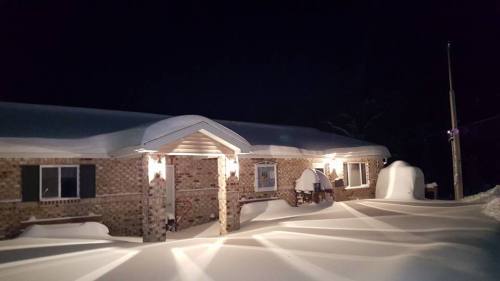A brick house at night, surrounded by deep snow, with lights illuminating the entrance and snow-covered landscape.