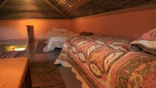 Cozy loft bedroom with two beds, warm lighting, and a rustic wooden ceiling.