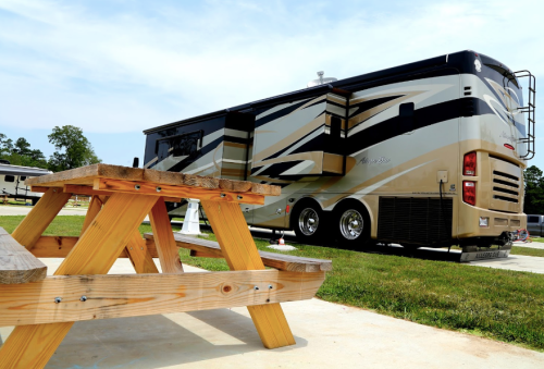 A parked RV with a stylish exterior next to a wooden picnic table on a grassy area.