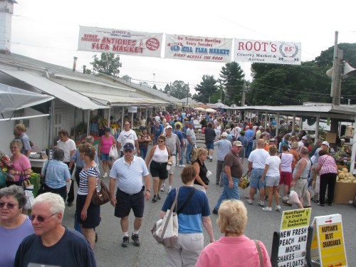 A bustling outdoor flea market with many people browsing stalls and vendors under a clear sky.
