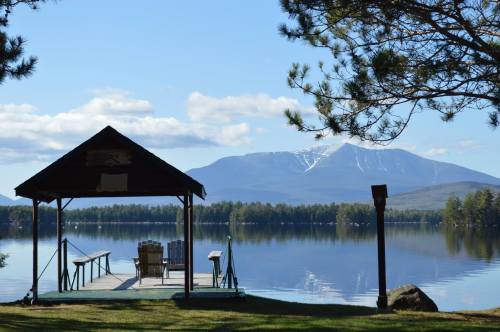 A serene lakeside view with a dock, chairs, and a mountain in the background under a clear blue sky.