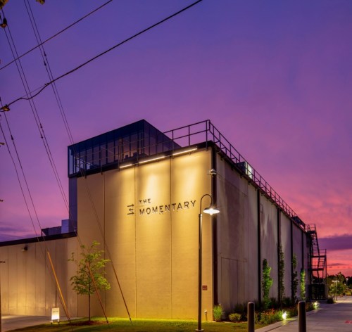 The Momentary building at dusk, illuminated under a colorful sky with trees and streetlights nearby.