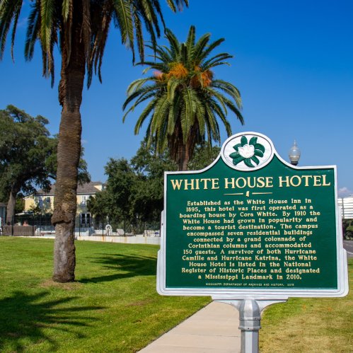 Historic sign for the White House Hotel, surrounded by palm trees, detailing its history and significance in Mississippi.