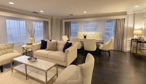 A modern living room with a white sofa, coffee table, and dining area featuring elegant chairs and large windows.