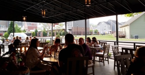 A lively outdoor dining area with people enjoying meals under a canopy, surrounded by houses in the background.