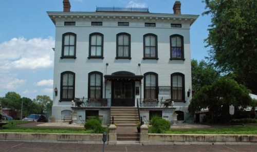 Historic white brick building with large windows, a staircase, and decorative ironwork, set against a blue sky.