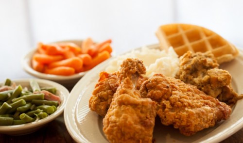 A plate of fried chicken with waffles, mashed potatoes, green beans, and carrots on the side.