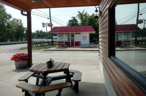 A picnic table outside a building, with a view of a small red-roofed kiosk and trees in the background.