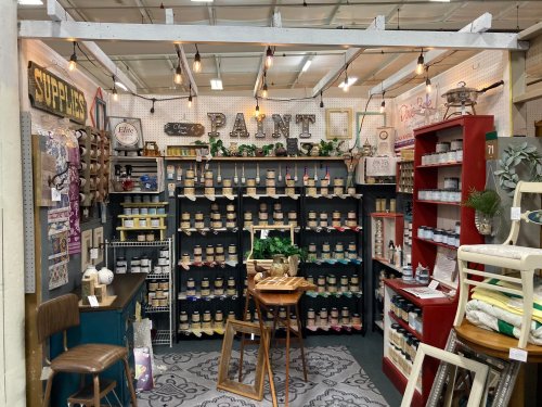 A cozy shop corner displaying paint cans, decor items, and a wooden table under warm string lights.