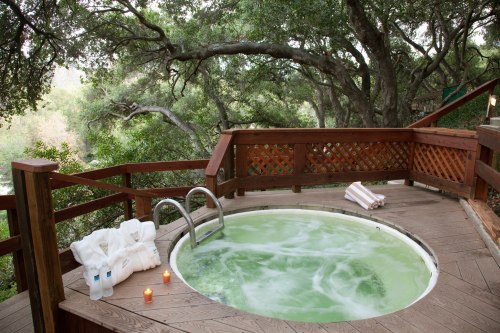 A serene outdoor hot tub surrounded by trees, with towels, candles, and a peaceful atmosphere.