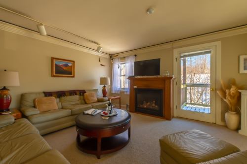 Cozy living room with a leather sofa, coffee table, fireplace, and large window overlooking a balcony.