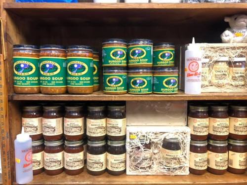 A wooden shelf displaying various jars of soup and sauces, labeled with colorful designs and logos.