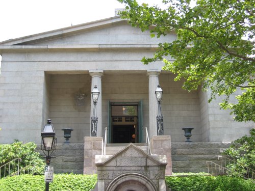A grand stone building with columns, steps, and decorative lanterns, surrounded by greenery.