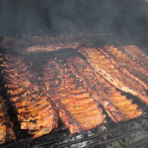 Smoky barbecue ribs sizzling on a grill, showcasing a rich, caramelized glaze and charred edges.