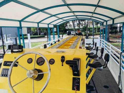 Interior of a yellow boat with a steering wheel and dashboard, featuring seating and a covered canopy.