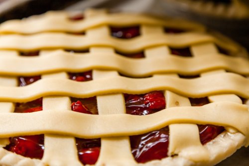 Close-up of a cherry pie with a lattice crust, revealing the glossy red filling underneath.