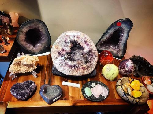 A display of various crystals and geodes, including amethyst, quartz, and colorful polished stones on a wooden table.
