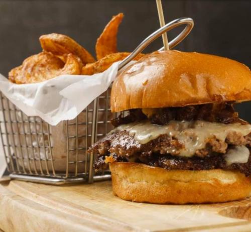 A juicy burger with melted cheese on a bun, served alongside a basket of crispy potato wedges.