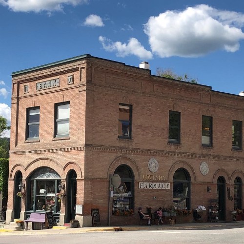 Historic brick building with arched windows, featuring a pharmacy sign and a blue sky with fluffy clouds above.