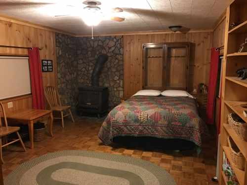 Cozy bedroom with wooden walls, a stone fireplace, a double bed, and a small dining table with chairs.