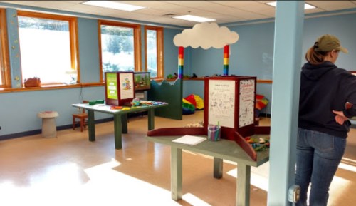 Brightly lit playroom with colorful decorations, tables with activities, and a person standing near the entrance.