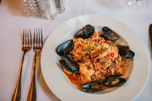 A plate of seafood paella with shrimp, mussels, and rice, garnished with vegetables, on a white tablecloth.