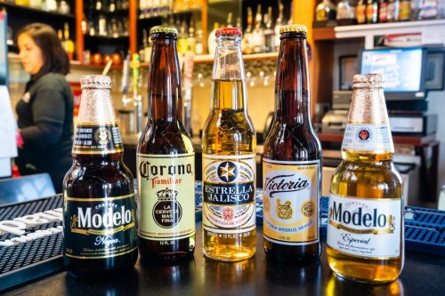 Five bottles of Mexican beer lined up on a bar: Modelo Negra, Corona Familiar, Estrella Jalisco, Victoria, and Modelo Especial.