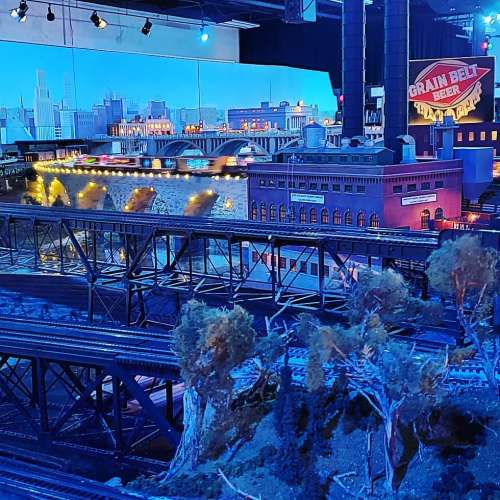 A detailed model train setup featuring buildings, bridges, and trees, illuminated with colorful lights.