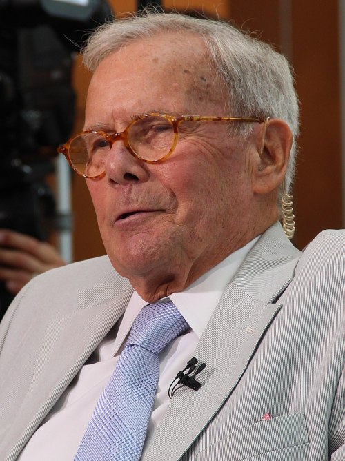 An elderly man with glasses and a light suit, speaking during an interview or event.