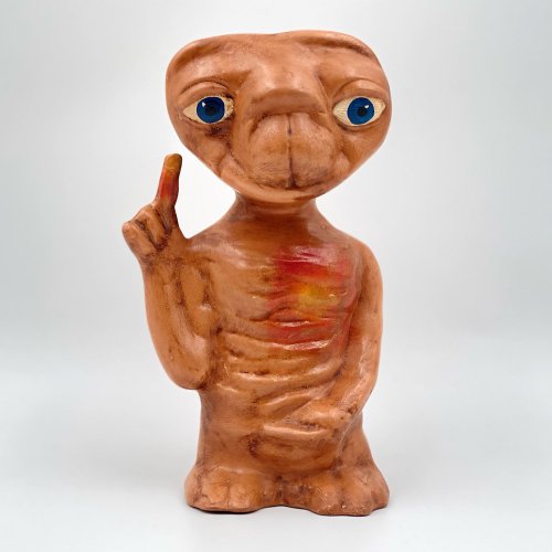A clay sculpture of a friendly alien with big blue eyes, a brown body, and one finger raised in a greeting gesture.