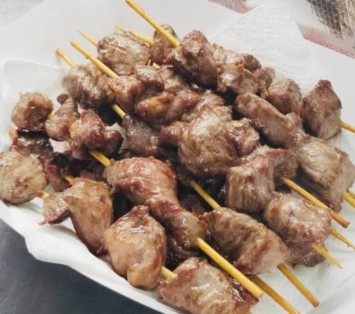A platter of grilled meat skewers arranged on a white paper towel.