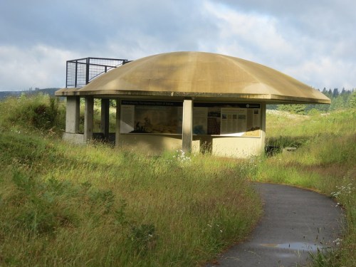 A round, concrete structure with a dome roof, surrounded by tall grass and a pathway leading to it.